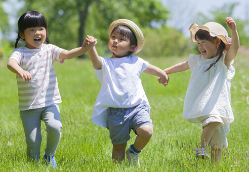 3人の幼児が手を繋いで元気よく笑顔で歩いている様子