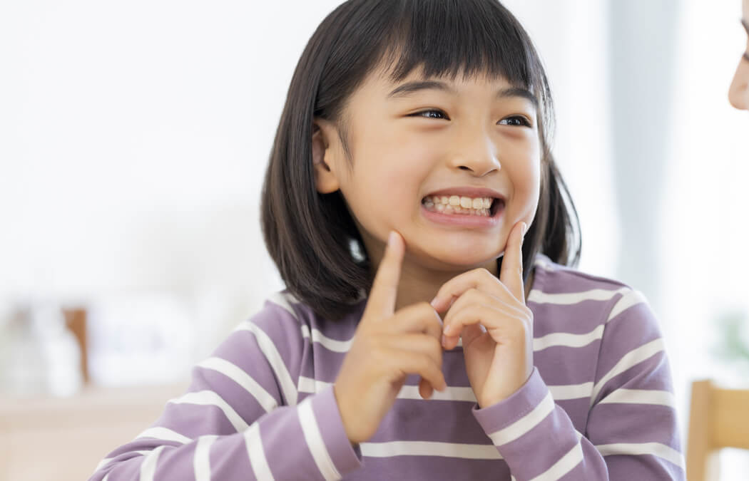 小学生くらいの子供が笑顔で自分の歯を指さしている様子